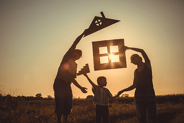 Happy family standing on the field at the sunset time. family in field holding up a house cut out